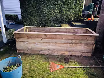 Timber garden bed in front of a hedge